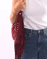 Bolso de hombro estilo boho confeccionado en gamuza color bordó. Presenta un diseño semicircular decorado con tachas metálicas plateadas dispuestas en líneas curvas y flecos largos en todo el borde inferior. Cuenta con cierre superior y correa ajustable para llevar al hombro.