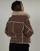 Campera tipo gamulán de cuero marrón con interior y solapas de piel sintética en color crema. Presenta un diseño de paneles con costuras visibles y cierre frontal.