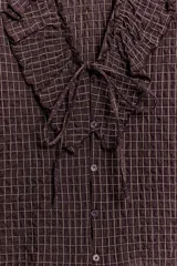 Camisa de manga larga con estampado de cuadros, escote en pico con volantes decorativos y cierre frontal con botones. Presenta puños elásticos.