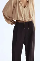 Pantalón de corte holgado en sarga color marrón oscuro. Modelo de tiro alto con trabilla ajustable de botón a ambos lados de la pretina, cierre con corchete oculto, piernas barrel con pinzas, pliegues adelante y atrás, bolsillos al bies y bolsillos traseros decorativos.