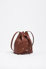 Bolso tipo bucket Bimba y Lola modelo Carlino, confeccionado en cuero marrón con estampado de pequeñas palmeras doradas y logo impreso en la parte frontal. Cuenta con cierre de cordón ajustable y asas largas para llevar al hombro.