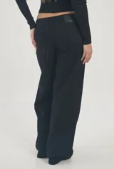 Jeans negros de tiro bajo y corte wide leg, con diseño de tachas metálicas plateadas a lo largo de las costuras laterales y delanteras.