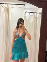 Vestido corto negro con estampado de plumas doradas, escote en V, breteles finos cruzados en la espalda, cut-outs laterales y volado en el ruedo.