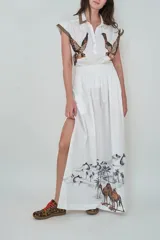 Falda maxi blanca de popelina de algodón, de corte fluido, con cintura elástica fruncida, tajo lateral en la pierna y estampado en el ruedo con diseño de desierto, palmeras y camellos.