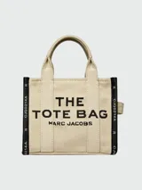 Bolso tipo tote de Marc Jacobs, confeccionado en tejido jacquard negro con detalles en color crema. Presenta el nombre del modelo estampado en el frente, doble asa superior y correa ajustable extraíble.