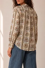 Camisa de manga larga color beige con estampado geométrico y floral en tonos marrones y naranjas, escote en V y botonadura frontal.