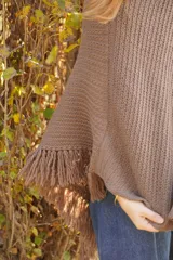 Poncho tejido en lana merino color marrón, con diseño de punto acanalado y terminación con flecos en el borde inferior. Incluye una pequeña etiqueta de cuero en la parte posterior.