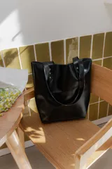 Cartera tipo tote bag de cuero marrón, con diseño minimalista, asas largas y detalles de remaches metálicos en la unión de las asas.