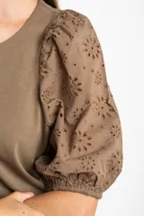 Remera de algodón color rosado con mangas cortas abullonadas de broderie con diseño floral calado. Presenta cuello redondo y costura vertical central en el frente.