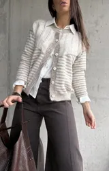 Cardigan de punto con diseño de rayas horizontales en tonos beige y blanco, cuello redondo y cierre frontal con botones. Presenta mangas largas con puños ajustados.