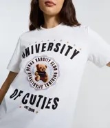 Remera de algodón color blanco, con cuello redondo y mangas cortas. Presenta un estampado frontal estilo universitario con el texto 'University of Cuties' y un oso en el centro.
