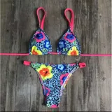 Conjunto de bikini United Uy modelo Mili, con estampado colorido de flores sobre fondo celeste con patrón de leopardo. El corpiño es de diseño triangular con tirantes fucsias y la bombacha es de corte tanga con detalles ajustables en los laterales.