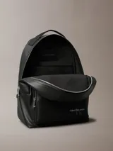Mochila negra de cuero sintético con asa de mano y tirantes ajustables. Tiene un bolsillo frontal con cierre y el logo de Calvin Klein Jeans estampado en la parte inferior.