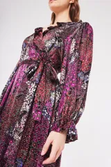 Vestido largo cruzado con estampado floral en tonos fucsia, rojo, blanco y azul sobre fondo negro. Presenta escote en V, cuello con volados y mangas largas abullonadas con puños elásticos. Incluye un lazo para ajustar en la cintura.
