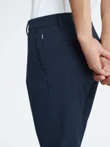 Pantalón chino de hombre, color azul marino, de corte slim y tiro medio. Presenta cierre frontal con botón y cremallera, trabillas para cinturón y bolsillos laterales y traseros.