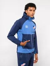 Campera deportiva Umbro del Club Nacional de Football, modelo Summit. Presenta un diseño con bloques de color en azul, rojo y blanco, con capucha, cierre frontal y bolsillos laterales con cierre. Incluye el logo de la marca y el escudo del club en el pecho.