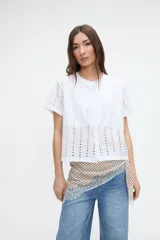 Blusa corta de broderie blanca, de manga corta, con cuello redondo y cierre frontal de botones.