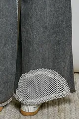 Pantalón de jean gris oscuro con corte holgado, parches asimétricos estilo patchwork con estampados de rayas y animal print en las rodillas, y detalle de tira central con botones a presión y encaje.