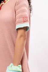 Vestido corto tejido de punto color salmón, con cuello redondo y mangas cortas. Presenta ribetes en color amarillo en el cuello, celeste en las mangas y naranja en el ruedo.