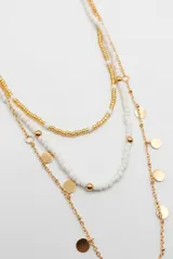Collar multicapa compuesto por una cadena metálica dorada con pequeños dijes circulares colgantes, una tira de cuentas blancas y una tira de cuentas doradas y blancas.