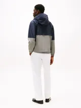 Campera deportiva Tommy Hilfiger para hombre, confeccionada en nylon, con diseño de bloques de colores azul marino y gris, capucha ajustable, cierre frontal con cremallera y logo bordado en el pecho.