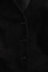 Chaleco negro de pana, con escote en V y cierre frontal de tres botones. Es una prenda entallada y forrada.