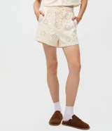 Short femenino de tiro alto color crudo, confeccionado en sarga con textura floral calada de broderie. Cuenta con cintura elástica y cordón ajustable para anudar.