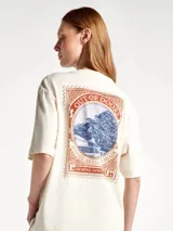 Camiseta de corte oversized color beige, con cuello redondo y mangas cortas. Presenta un estampado frontal con diseño de palmeras y texto en tonos azul y bordó con efecto desgastado.