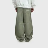 Pantalón de jean estilo baggy, de corte ultra holgado y tiro medio. Presenta un tono verde lavado con efecto desgastado, bolsillos traseros amplios y un bordado decorativo con llamas y texto en uno de los bolsillos.