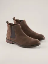Bota Chelsea de gamuza gris con elásticos laterales, suela de goma marrón y tirador trasero.