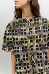 Camisa de popelina de algodón con cuello mao, botones frontales agrupados en pares y mangas cortas abullonadas tipo balloon. Cuenta con un diseño estampado de patrón geométrico y floral sobre fondo negro.