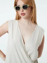 Vestido corto color beige, cruzado, sin mangas y ajustable con lazo lateral.