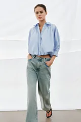 Camisa de algodón con cuello solapa, mangas abullonadas por debajo del codo y bajo acabado en globo. Presenta cierre frontal con botones ocultos.