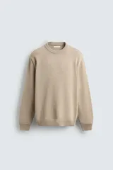 Sweater de punto color beige, de corte regular fit, con cuello redondo y manga larga. Presenta terminaciones en rib en cuello, puños y dobladillo.
