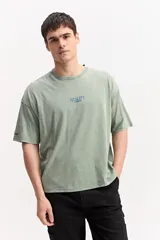 Remera oversize color verde militar con efecto acid wash, cuello redondo y pequeño estampado frontal con la inscripción "REALITY".