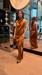 Vestido largo de satén con escote drapeado y espalda descubierta. Presenta un corte fluido y elegante con una abertura lateral en la falda.