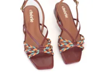 Sandalia de cuero color caramelo, con tiras finas y detalle frontal trenzado en tonos marrón, celeste y naranja. Cuenta con pulsera ajustable con hebilla metálica y taco bajo geométrico.