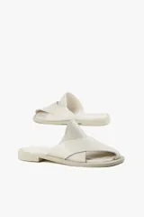 Sandalias planas de cuero color blanco hueso, con dos tiras anchas cruzadas en la parte superior y diseño minimalista.