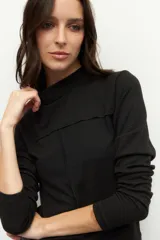 Polera negra de manga larga con cuello alto y costuras a la vista en el frente.