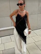 Vestido negro de satén con encaje en escote y ruedo, de corte asimétrico y breteles finos.