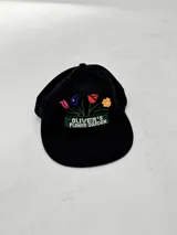 Gorro tipo gorra de béisbol color negro con visera curva. Presenta un bordado frontal de un macetero con flores de colores (rosa, azul, rojo y naranja) y el texto "OLIVER'S FLOWER GARDEN" en blanco sobre un fondo verde.