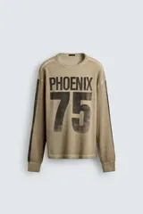 Sudadera de corte relajado confeccionada en tejido con textura waffle, color beige con efecto lavado. Presenta cuello redondo, manga larga con franjas laterales oscuras y estampado frontal con texto y número en contraste.