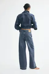 Jean de tiro alto confeccionado en denim de algodón rígido, con diseño de cinco bolsillos, perneras amplias y corte holgado. Presenta un lavado azul medio y detalle de dobladillo deshilachado.