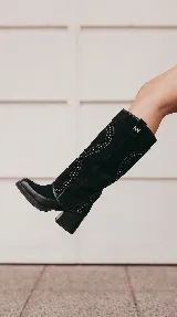 Bota alta de gamuza negra con diseño western, caña desmontable, taco ancho y detalles de tachas aplicadas.