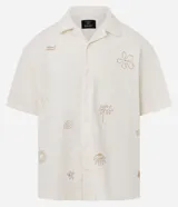 Camisa masculina boxy de manga corta en tricolina color marfil, con cuello cubano, cierre frontal con botones y sutiles bordados veraniegos en tono tostado.