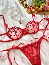 Conjunto de lencería rojo de dos piezas, confeccionado en tul semitransparente con bordados de corazones. Incluye corpiño con copa armada y bombacha colaless ajustable con tiras laterales terminadas en lazo.