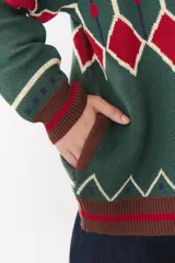 Campera tipo bomber tejida con diseño jacquard geométrico en tonos azul marino, blanco, rojo y verde. Presenta cierre frontal completo, cuello, puños y ruedo acanalados en color verde y blanco, con corte oversized y hombros caídos.