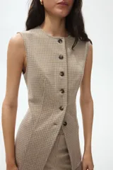 Chaleco largo sin mangas con cuello redondo y cierre frontal de botones. Presenta un diseño de tejido jacquard con patrón de cuadros pequeños y costuras verticales que definen la silueta.