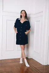Vestido camisero de corte holgado, color azul marino, con cuello camisero en tono gris claro, cierre frontal completo con botones y mangas cortas. Presenta un diseño funcional ideal para maternidad y lactancia.