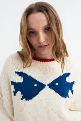 Sweater de punto color rosado con diseño jacquard de peces azules en el pecho, cuello redondo, puños y ruedo en tono rojo contrastante. Presenta textura en rombos y mangas largas holgadas.